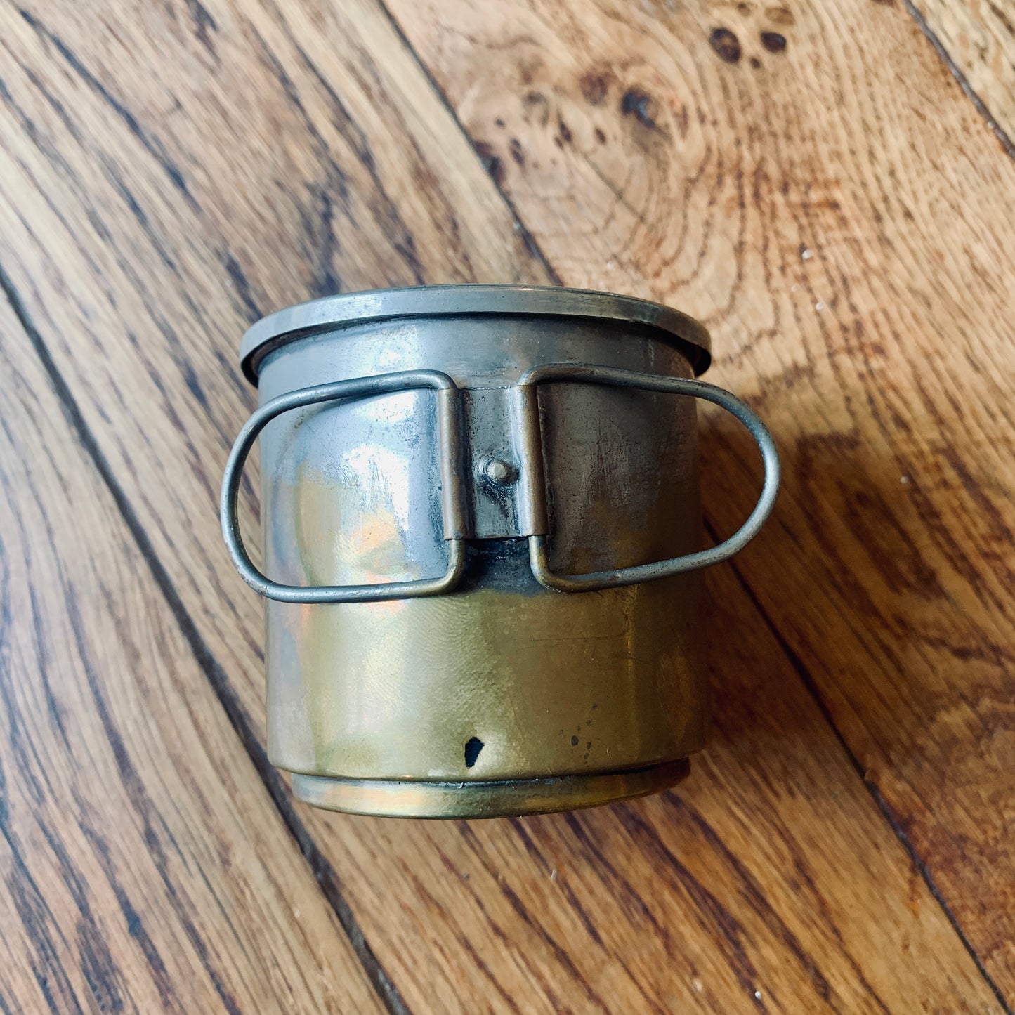 Tazza da campeggio in metallo con manico pieghevole su una superficie in legno.