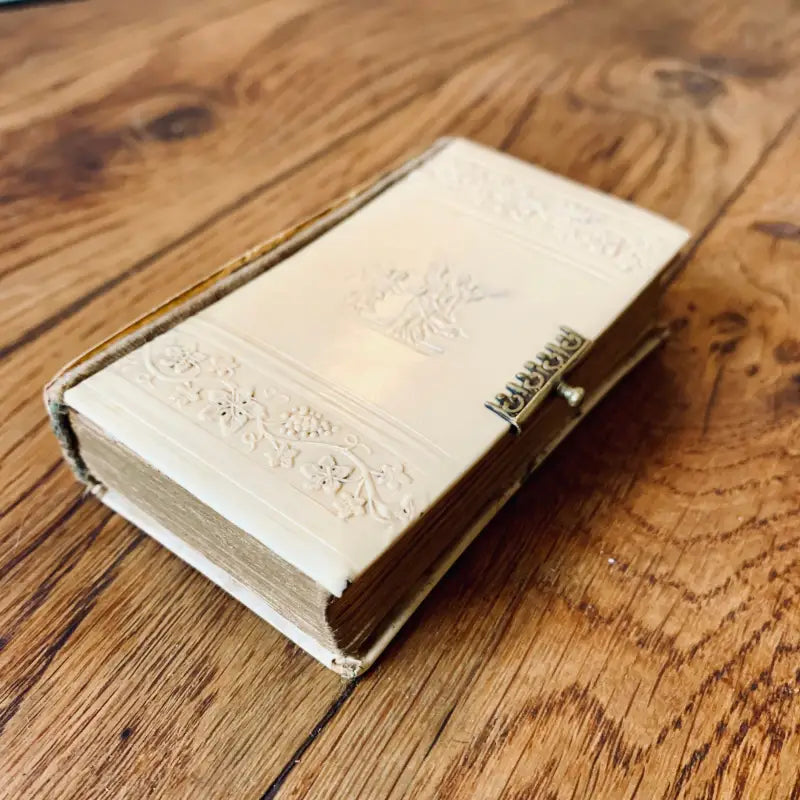 Libro bianco ornato con chiusura dorata adagiato su una superficie di legno.