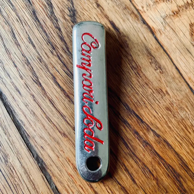 Apribottiglie grigio metallizzato con scritta ’Campari soda’ in rosso.