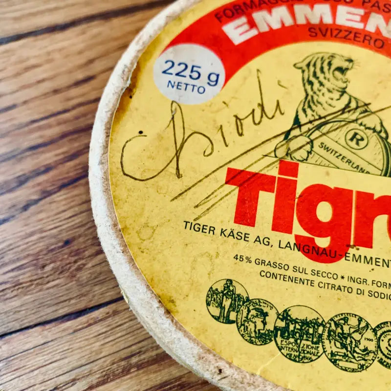 Forma rotonda con etichetta gialla e rossa con i marchi ’Emmentaler’ e ’Tigre’.