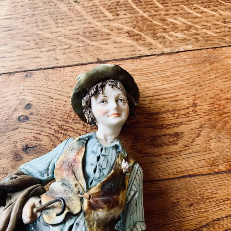 Statuetta in ceramica di un ragazzo sorridente che indossa un berretto e abiti colorati.