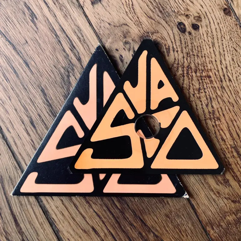Toppa o emblema triangolare con disegno geometrico astratto in arancione e nero.