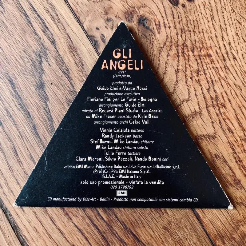 Oggetto triangolare nero con testo dorato che elenca i nomi, probabilmente un inserto per i crediti di un album o di un film.