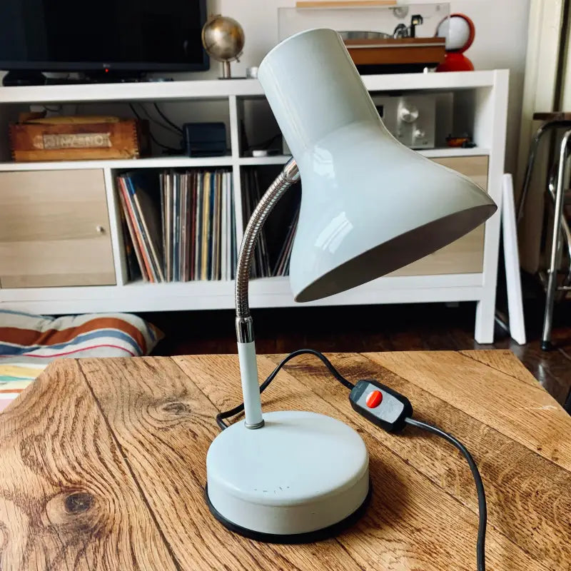 Lampada da tavolo regolabile di colore blu pallido con paralume conico su una superficie in legno.
