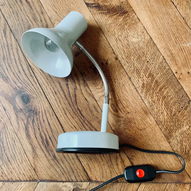 Lampada da tavolo regolabile con collo flessibile e base rotonda su una superficie in legno.