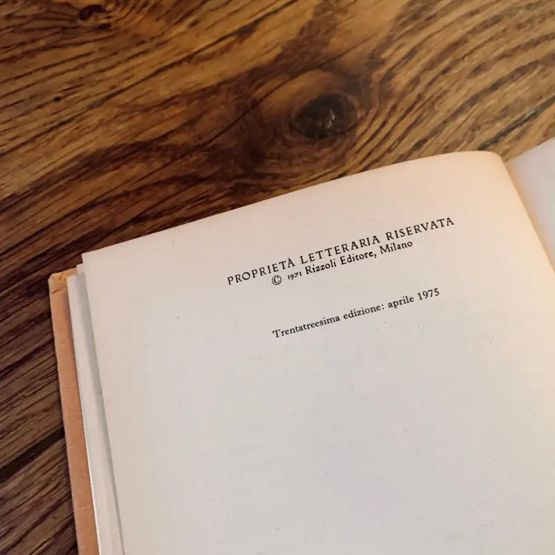 Libro con testo italiano sul frontespizio, appoggiato su una superficie di legno.