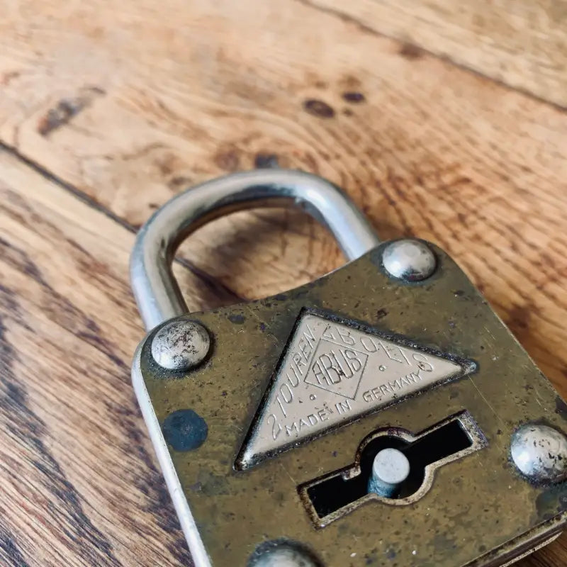 Lucchetto in ottone antico con foro per la chiave triangolare su una superficie di legno.