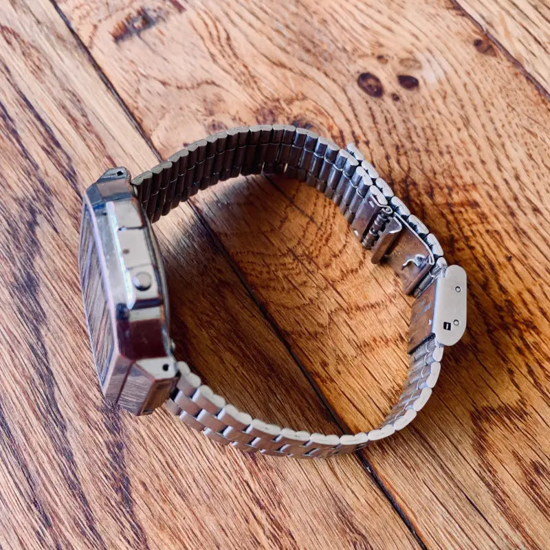 Orologio da polso in metallo con cinturino espandibile appoggiato su una superficie di legno.