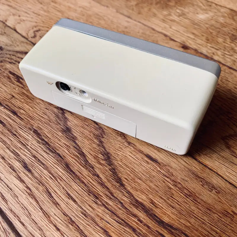Dispositivo elettronico bianco rettangolare con una piccola lente su un lato, probabilmente un altoparlante o una fotocamera portatile.