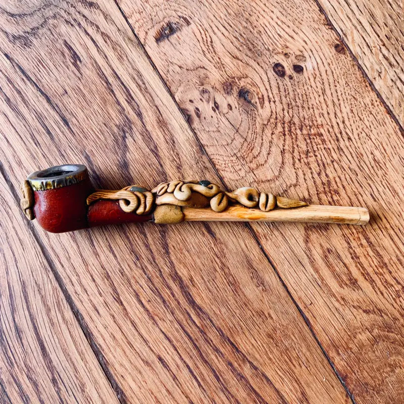 Pipa in legno ornata con disegni intagliati e una ciotola rossa.