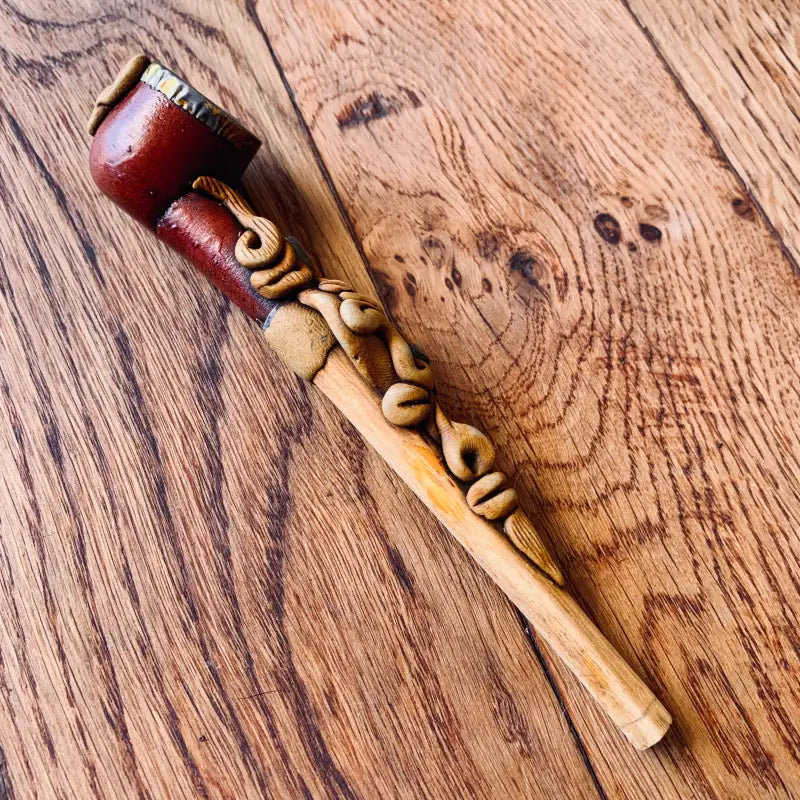 Pipa in legno ornata e intagliata con una ciotola marrone rossastra.