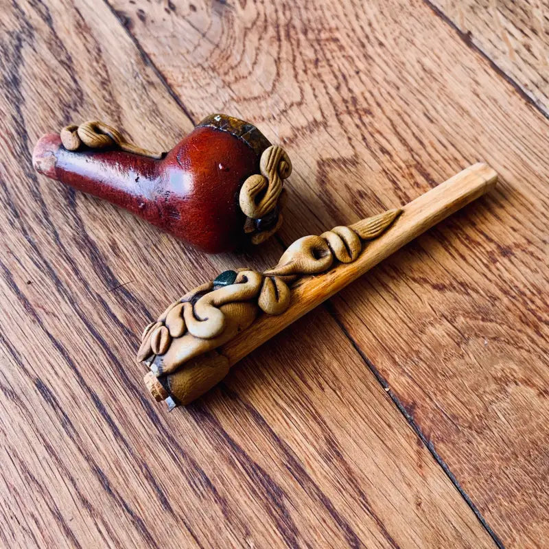 Due pipe da fumo decorative, una rossa e una di legno, ornate con disegni intagliati e piccole perline.
