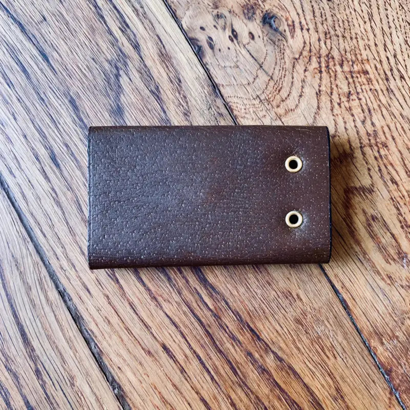 Portafoglio o portacarte in pelle marrone con due occhielli in metallo.