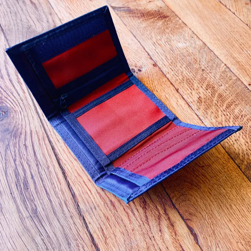 Portafoglio aperto blu con scomparti interni rossi su una superficie di legno.