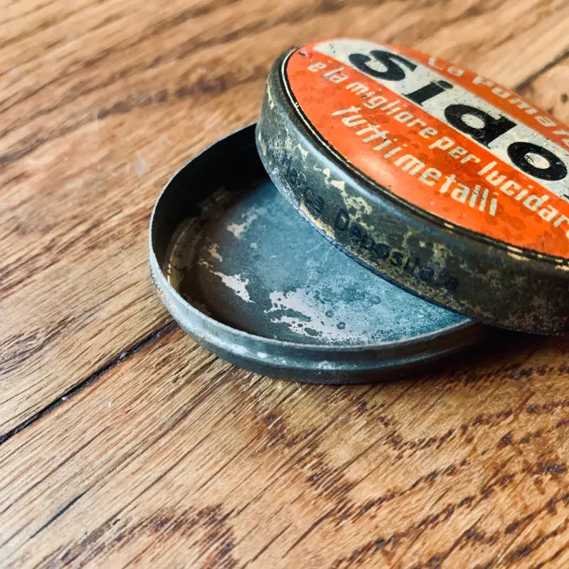 Scatola di metallo vintage di pastiglie per la gola Sida con coperchio arancione, parzialmente aperta su una superficie di legno.