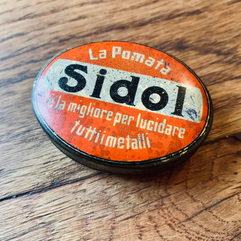 Barattolo vintage di metallo arancione e bianco di smalto Sidol su una superficie di legno.