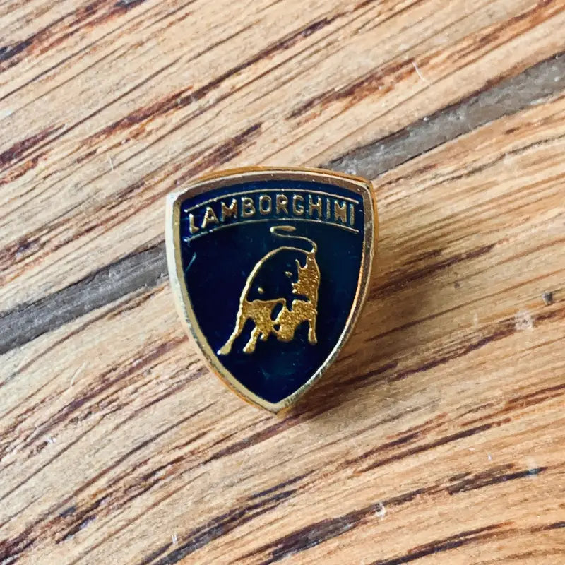 Stemma con logo Lamborghini con toro dorato su sfondo blu scuro a forma di scudo.