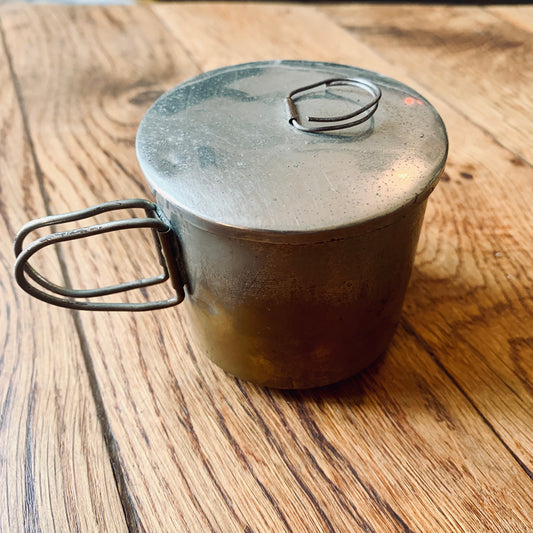 Tazza da campeggio in metallo con coperchio e manico in filo metallico.