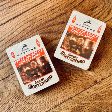 Due carte da gioco con il marchio Amaro Montenegro su una superficie di legno.