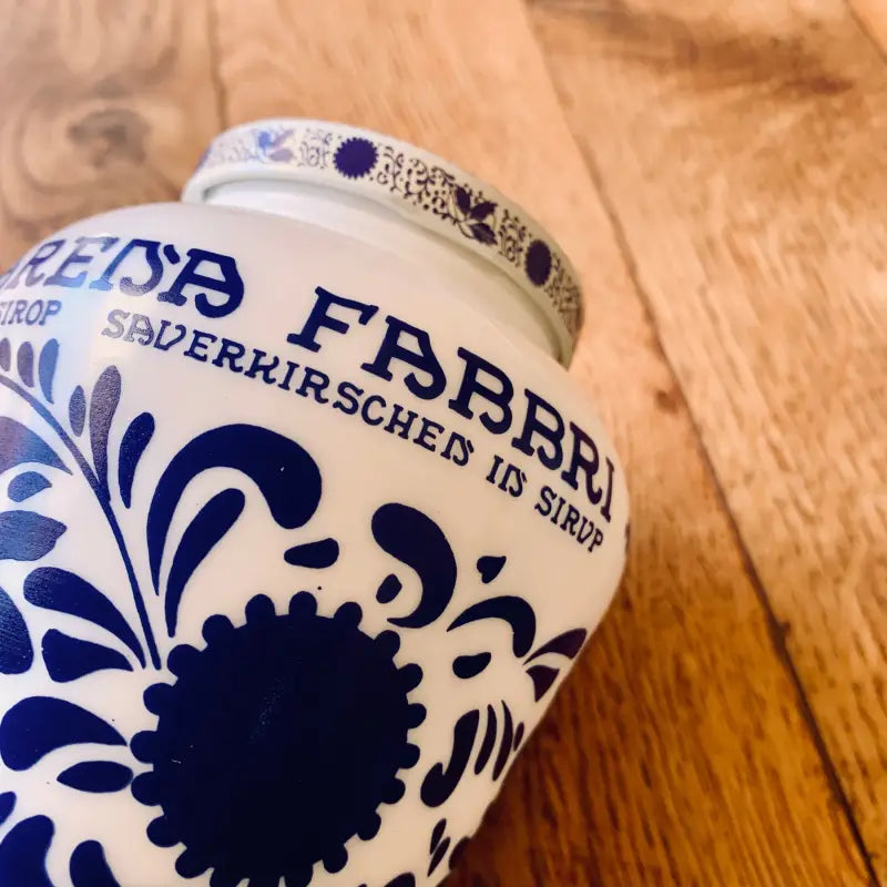 Vaso o contenitore in ceramica con disegni floreali e testo blu, probabilmente per conservare alimenti o bevande.