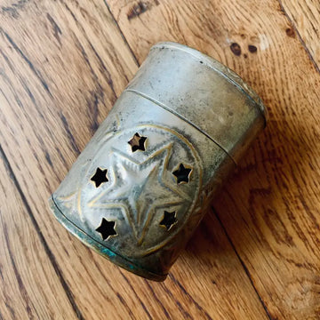 Tazza o contenitore di metallo con ritagli a forma di stella sulla superficie.