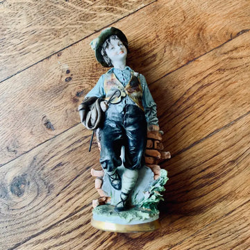 Statuetta in porcellana di un ragazzo in abiti d’epoca su una base decorativa.