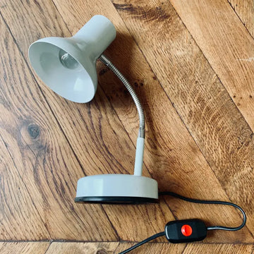 Lampada da tavolo regolabile con collo flessibile e base rotonda su una superficie in legno.