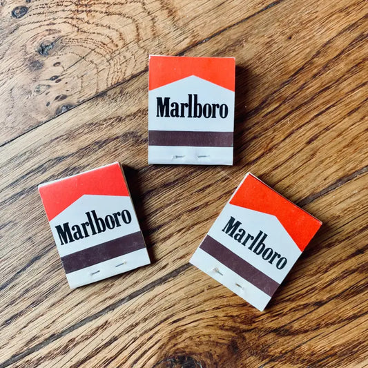 Tre pacchetti di sigarette Marlboro disposti su una superficie di legno.
