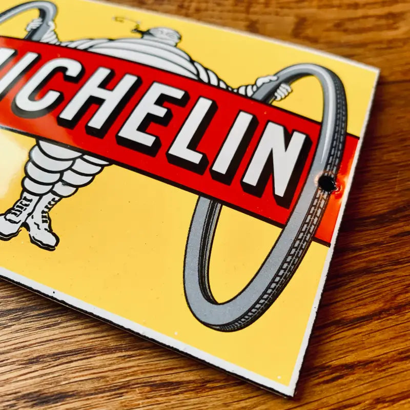 Cartello pubblicitario d’epoca per pneumatici Michelin con l’iconica mascotte dell’omino Michelin e un pneumatico.