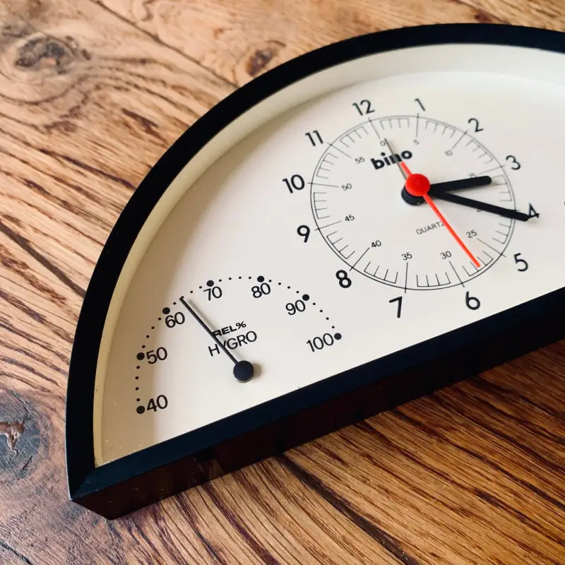 Orologio a semicerchio con indicatori di temperatura e umidità su una superficie di legno.