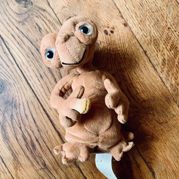 Peluche di E.T. l’Extra-Terrestre adagiato su una superficie di legno.