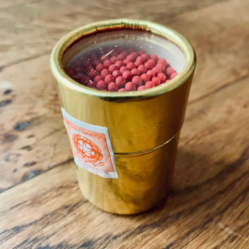 Tazza di ceramica dorata contenente un liquido scuro con oggetti sferici rossi che galleggiano sopra.