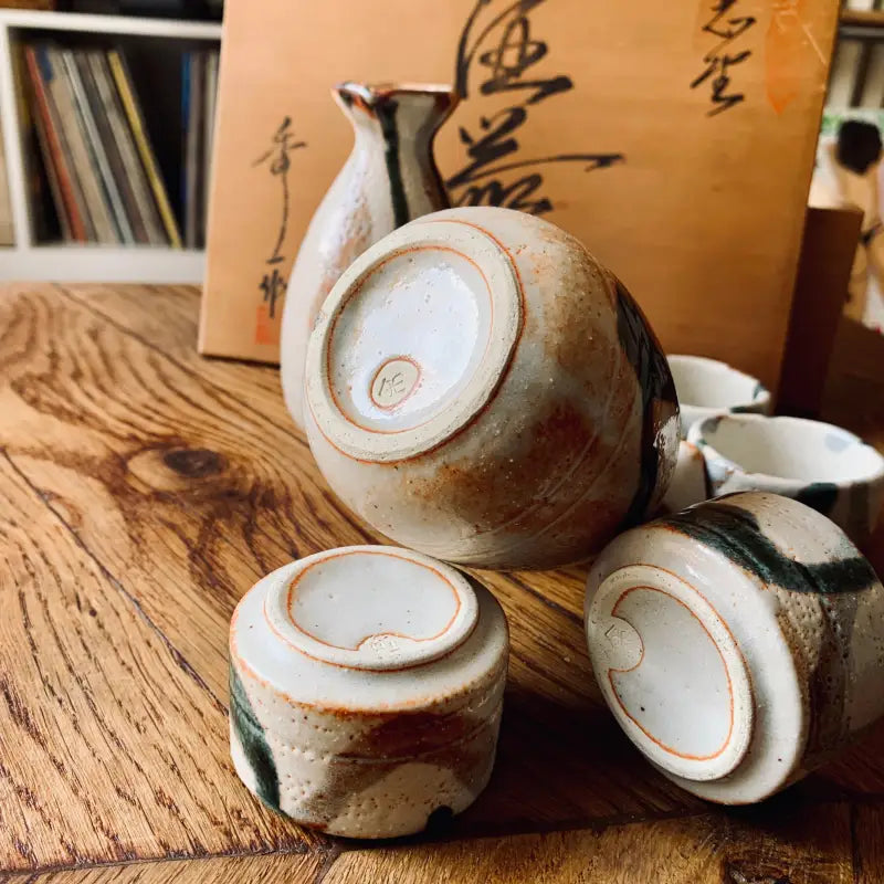 Set da sakè in ceramica con bottiglia e tazze su una superficie di legno.