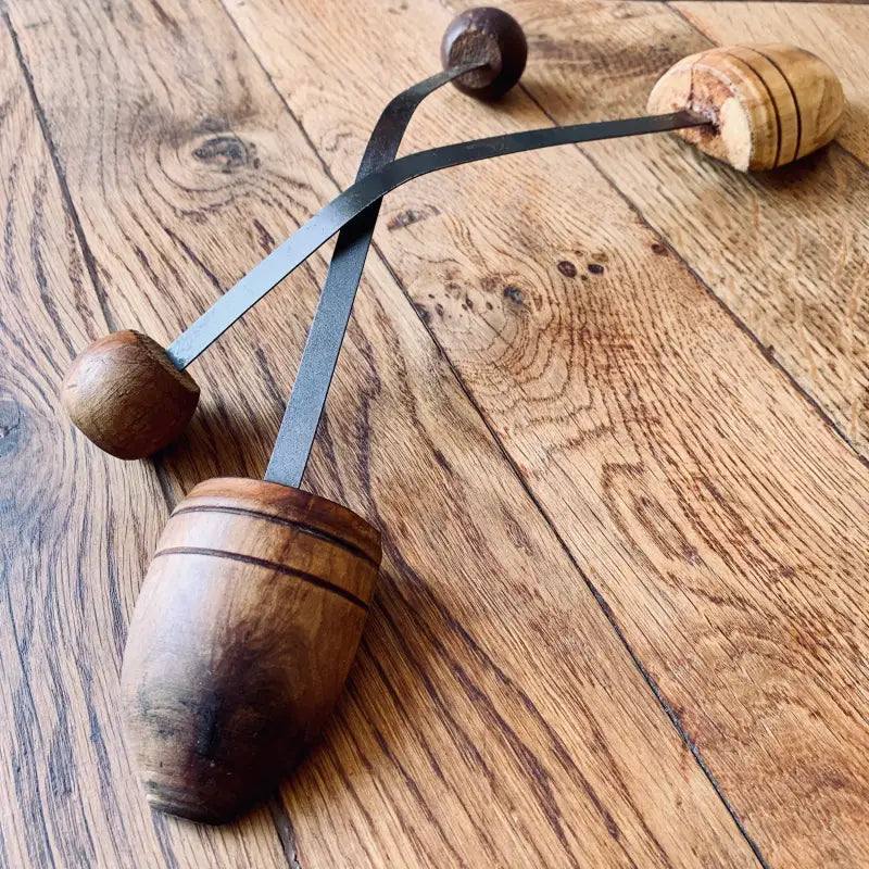 Strumento a percussione in legno con due sfere collegate su cinghie di cuoio.